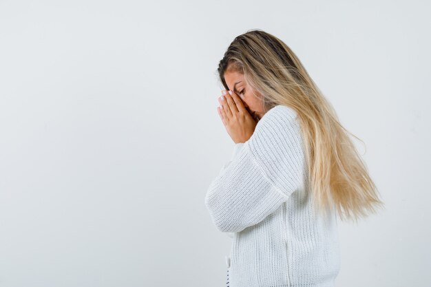 Blondes Mädchen im gestreiften T-Shirt, in der weißen Strickjacke und in der Jeanshose, die Hände in der Gebetsstellung fassen und fokussierte Vorderansicht schauen.