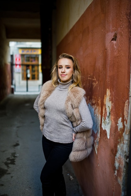 Kostenloses Foto blondes mädchen im pelzmantel posierte gegen alte orangefarbene wand