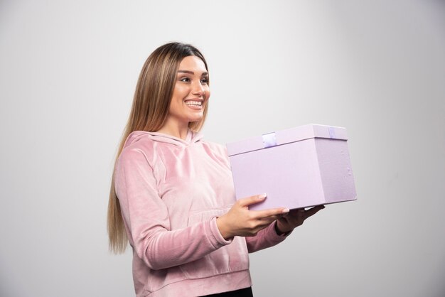 Blondes Mädchen im Sweatshirt erhielt eine Geschenkbox und fühlt sich positiv überrascht