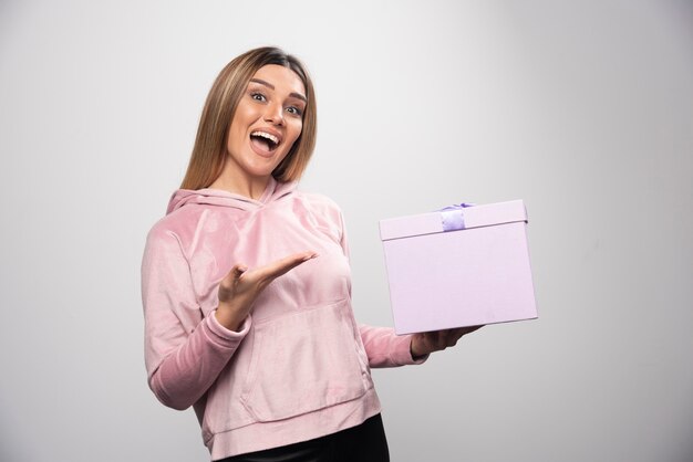Blondes Mädchen im Sweatshirt erhielt eine Geschenkbox und fühlt sich positiv überrascht