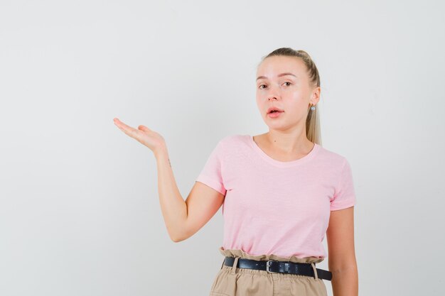 Blondes Mädchen im T-Shirt, Hose, die etwas begrüßt oder zeigt, Vorderansicht.