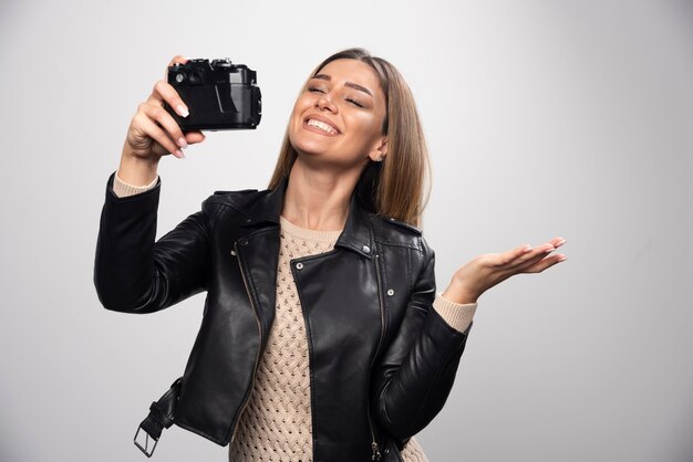 Blondes Mädchen in der schwarzen Lederjacke, die ihre Selfies mit einer Kamera nimmt.