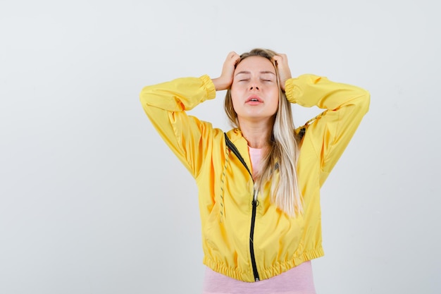 Blondes Mädchen in gelber Jacke, das die Hände am Kopf hält und genervt aussieht looking