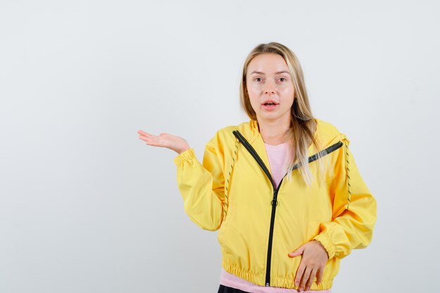 Blondes Mädchen in gelber Jacke macht Willkommensgeste und sieht verführerisch aus