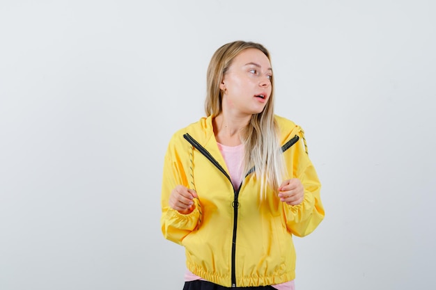 Kostenloses Foto blondes mädchen in gelber jacke posiert, während sie beiseite schaut und hübsch aussieht