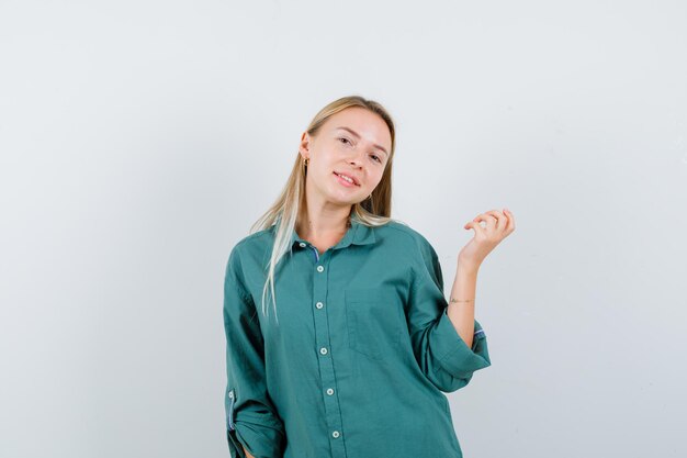 Blondes Mädchen in grüner Bluse, das eine Hand ausdehnt, als etwas hält und glücklich aussieht