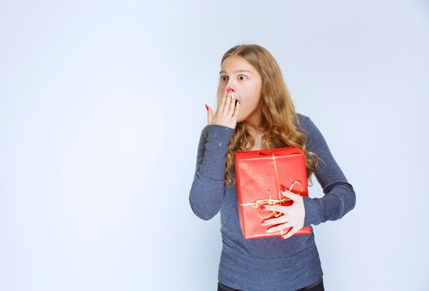 Blondes Mädchen mit einer roten Geschenkbox sieht verwirrt und verängstigt aus.