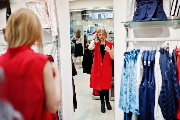 Blondes Mädchen probiert ein rotes Kleid in der Boutique an und schaut in den Spiegel