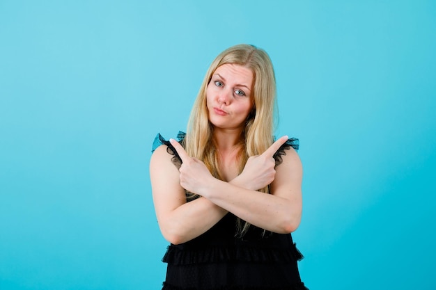 Kostenloses Foto blondes mädchen schaut in die kamera, indem sie die hände auf blauem hintergrund kreuzt