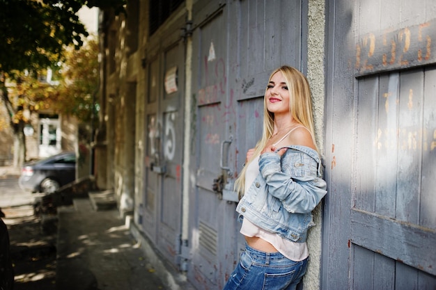 Kostenloses Foto blondes mädchen trägt eine jeansjacke, die auf der straße posiert