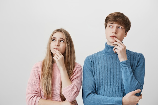 Blondes Mädchen und Kerl schauen in die obere linke Ecke, denken nach und treffen eine Entscheidung