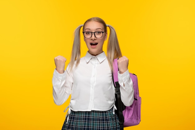 Blondes Mädchen zum Weltbuchtag mit Pferdeschwänzen und rosafarbenem Rucksack in Uniform