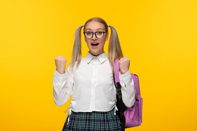 Blondes Mädchen zum Weltbuchtag mit Pferdeschwänzen und rosafarbenem Rucksack in Uniform