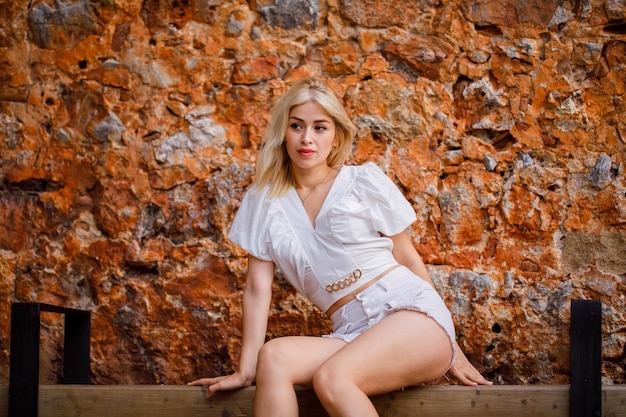 Blondes schönes Mädchen schaut weg, indem es auf einer Bank auf Steinhintergrund sitzt