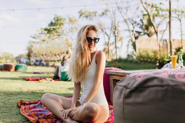 Blondhaarige wunderschöne Frau, die auf dem Boden im Park sitzt.