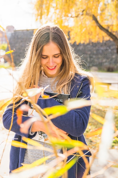 Blondine, die Buch im Herbstpark umarmen