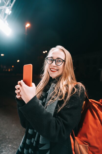 Blondine mit Smartphone nachts in der Straße.