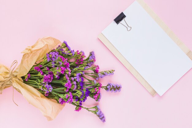 Blühen Sie den Blumenstrauß, der im braunen Papier nahe dem weißen leeren Papier auf Klemmbrett eingewickelt wird