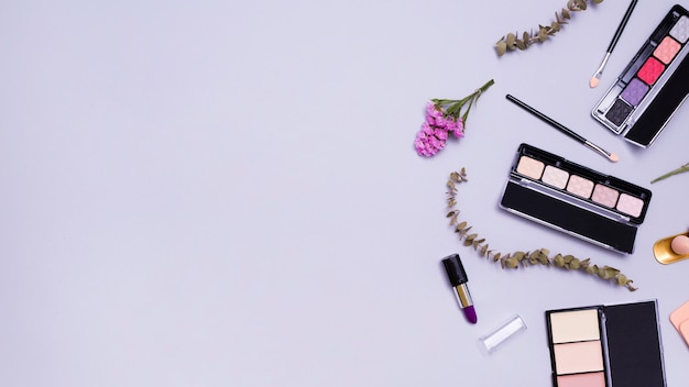 Blumen und Zweige mit Lippenstiften; Make-up Pinsel; Lippenstift; kompakte Pulver- und Lidschatten-Palette auf violettem Hintergrund
