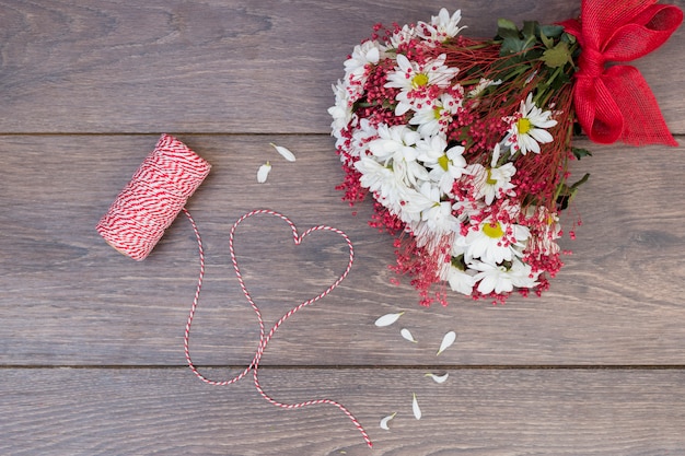 Blumenblumenstrauß mit Herzen vom Seil auf Holztisch