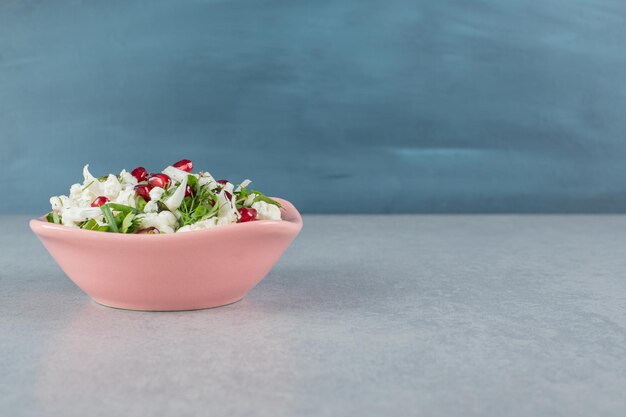 Blumenkohlsalat mit roten Granatapfelkernen in einem Teller.