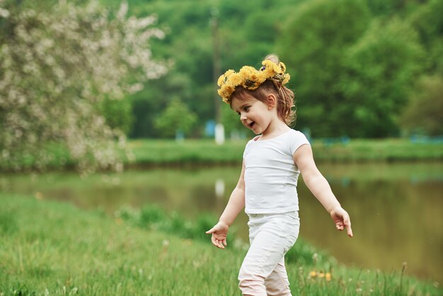 Blumenkranz ist auf dem Kopf. Kind, das Spaß hat, zur Frühlingszeit draußen zu gehen