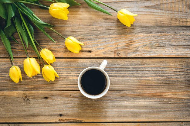 Blumenstrauß aus gelben Tulpen und einer Tasse Kaffee auf einem hölzernen Hintergrund, Draufsicht