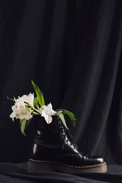 Blumenstrauß aus weißen Blüten mit grünen Blättern im dunklen Stiefel