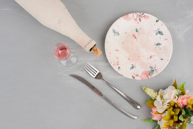 Blumenstrauß, ein Glas Roséwein und ein Teller auf grauer Oberfläche