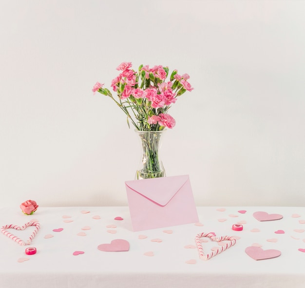 Blumenstrauß von Blumen im Vase nahe Satz Papierherzen, Umschlag und Zuckerstangen