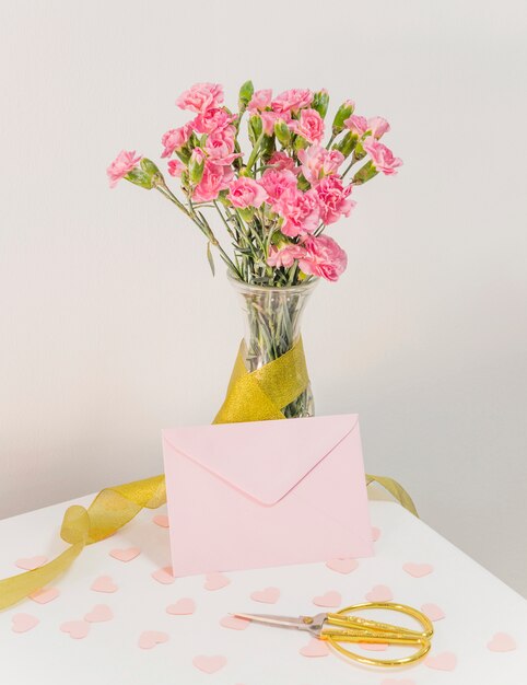 Blumenstrauß von Blumen in der Vase mit Band nahe Umschlag, Scheren und Papierherzen