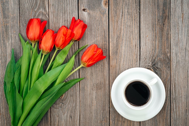 Kostenloses Foto blumenstrauß von roten tulpen und von einer tasse kaffee auf einer draufsicht des hölzernen hintergrundes