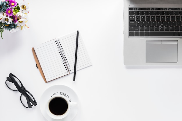 Blumenvase; Brille; Tagebuch; Bleistift und Kaffeetasse mit Laptop auf weißem Hintergrund