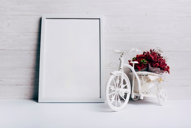 Blumenvase mit Fahrrad nahe dem weißen leeren Rahmen auf Schreibtisch