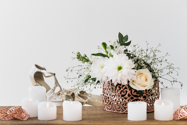 Blumenvase nahe den brennenden Kerze- und Hochzeitsschuhen gegen weißen Hintergrund
