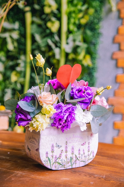 Blumenzusammensetzung in Papierbox cremige Rosen lila und weißer Lithianthus