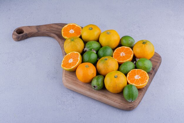 Board mit einem Haufen Mandarinen und Feijoas auf Marmorhintergrund. Foto in hoher Qualität