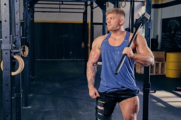 Bodybuilder mit verletztem Bein im Verband hält Langhantel in der Nähe von Cross-Fit-Ständer in einem Fitnessstudio.