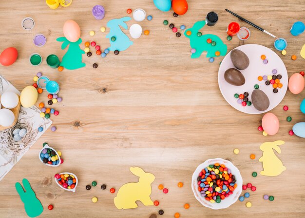 Bonbons mit bunten Edelsteinen; Ostereier; Farben und Pinsel auf Schreibtisch aus Holz