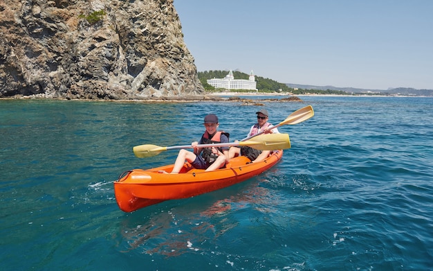 Boot Kajakfahren in der Nähe von Klippen an einem sonnigen Tag. Kajak fahren in einer ruhigen Bucht. Erstaunliche Aussichten. Reise-, Sportkonzept. Lebensstil. Eine glückliche Familie.