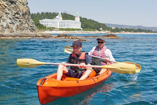 Boot Kajakfahren in der Nähe von Klippen an einem sonnigen Tag. Kajak fahren in einer ruhigen Bucht. Erstaunliche Aussichten. Reise-, Sportkonzept. Lebensstil. Eine glückliche Familie.