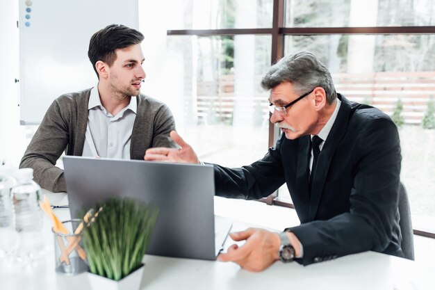 Boss mit seinen neuen Mitarbeitern im modernen Büro, die über Präsentation mit Laptop sprechen.