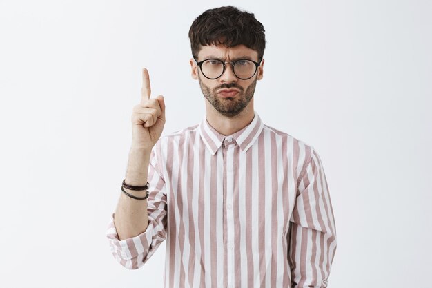 Bossy stilvoller bärtiger Kerl, der mit Brille gegen die weiße Wand aufwirft