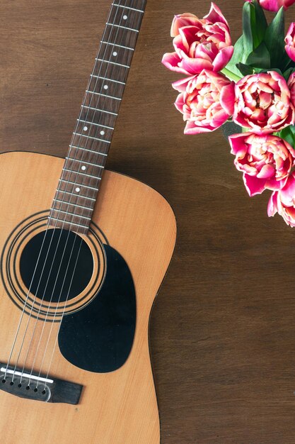 Bouquet aus rosa Tulpen und Akustikgitarre auf einem hölzernen Hintergrund