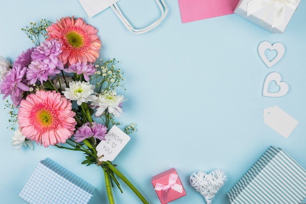 Bouquet von frischen Blumen mit Titel auf Tag in der Nähe von Paket, Geschenkkartons und Dekorationen