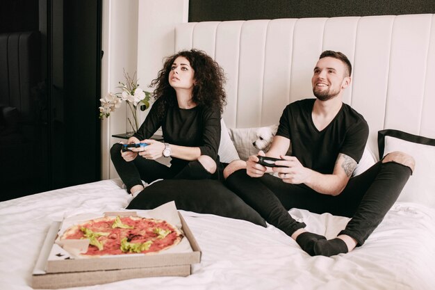 Box mit Pizza steht vor Mann und Frau spielen auf PS auf dem Bett
