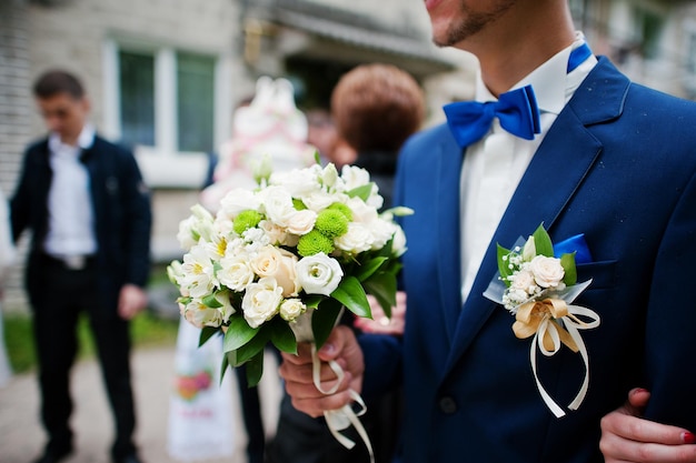 Bräutigam an blauer Jacke und Fliege mit Blumenstrauß