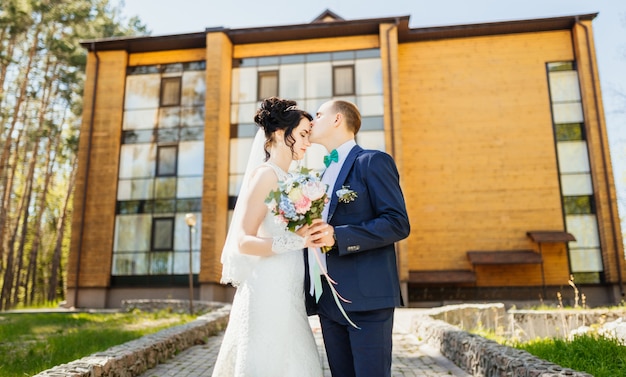 Bräutigam küsst die Braut auf der Stirn nach Hochzeitszeremonie gegen ein großes Holzhaus