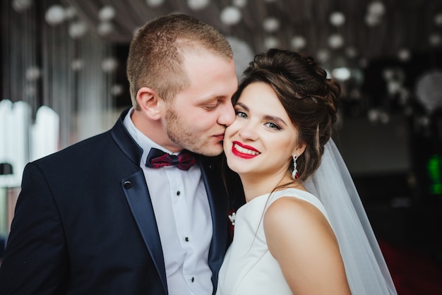 Bräutigam küsst lächelnde und glückliche Braut nach Hochzeitszeremonie