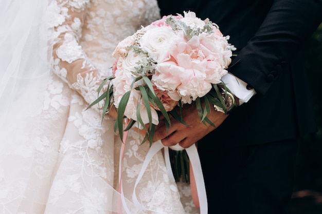Bräutigam und Braut halten Hochzeitsrosa-Blumenstrauß zusammen